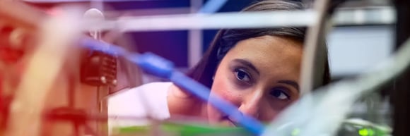 Technician closely inspecting robotic equipment, viewed through a frame of cables and machine components